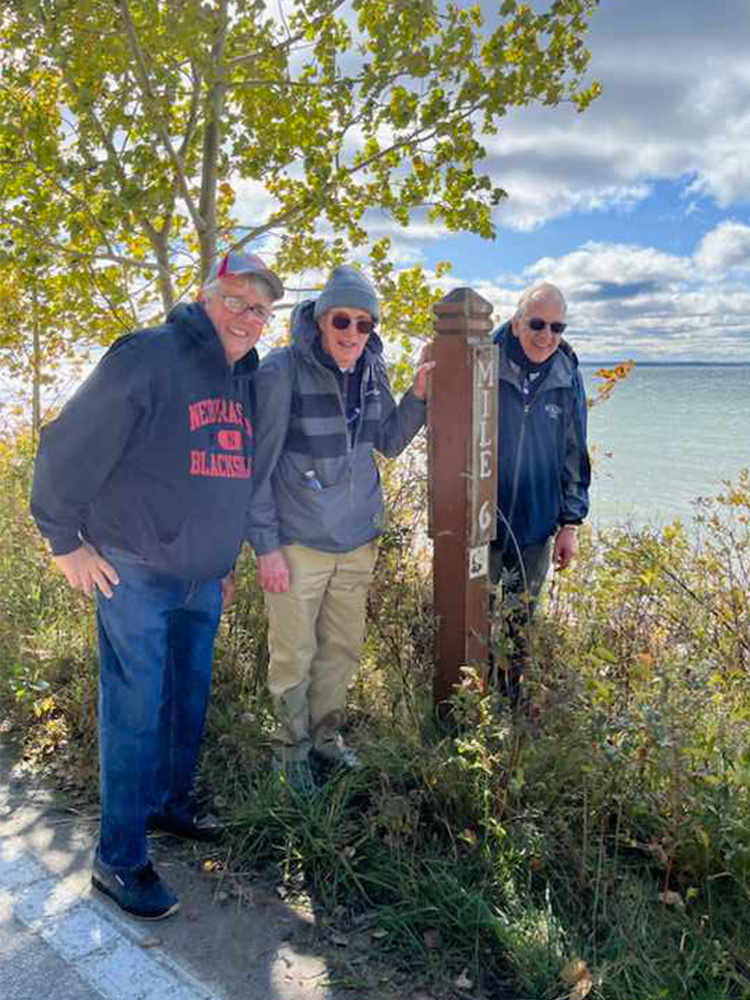 three older mean posing near a hiking sign and smiling